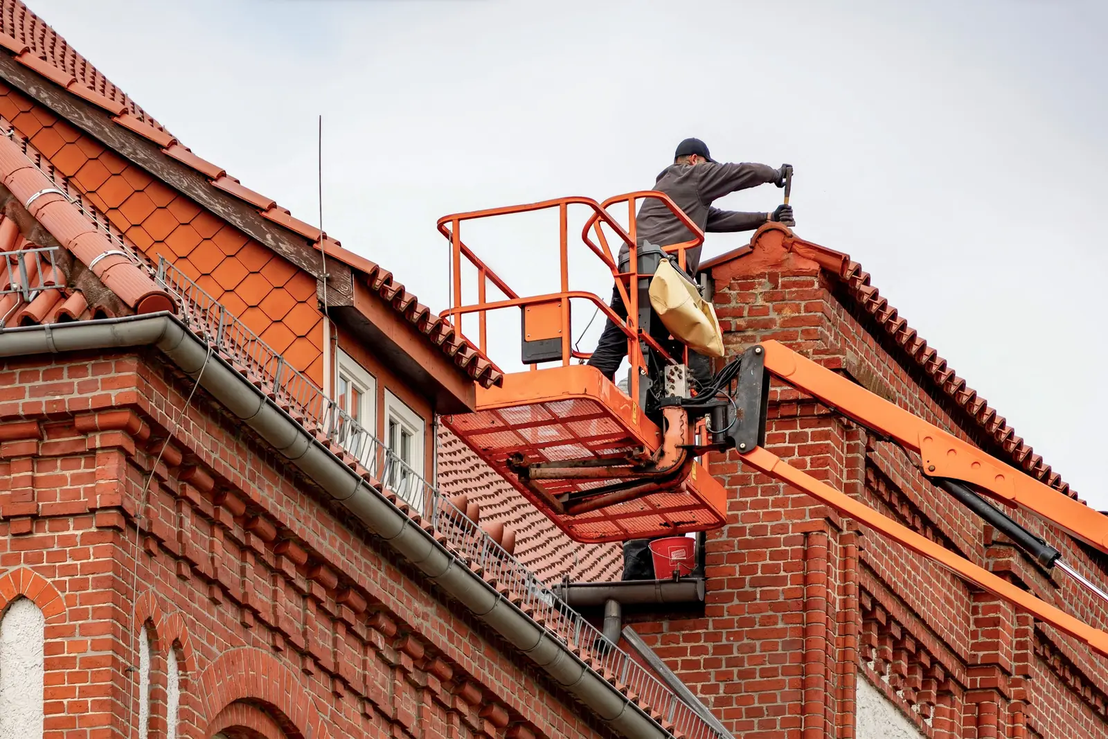 Dachhandwerker arbeitet von einer Hubarbeitsbühne aus an der Dachrinne eines Backsteingebäudes