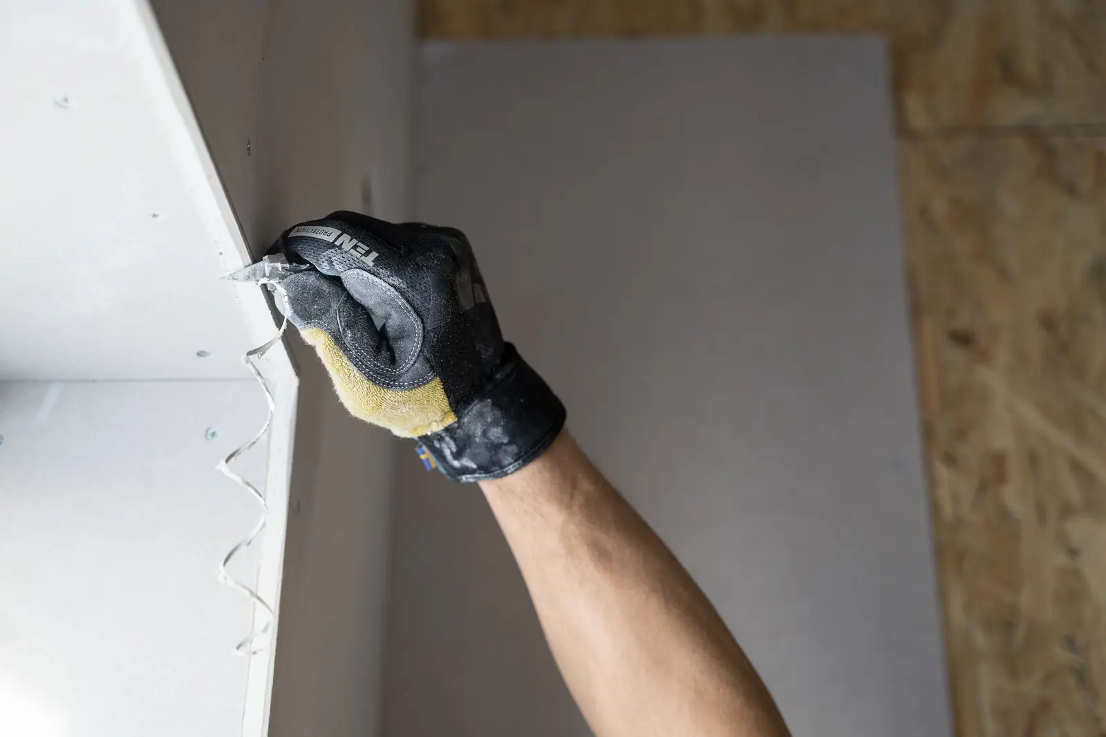 Behandschuhte Hand trägt mit einem Spachtel Fugenmasse auf Gipskarton auf