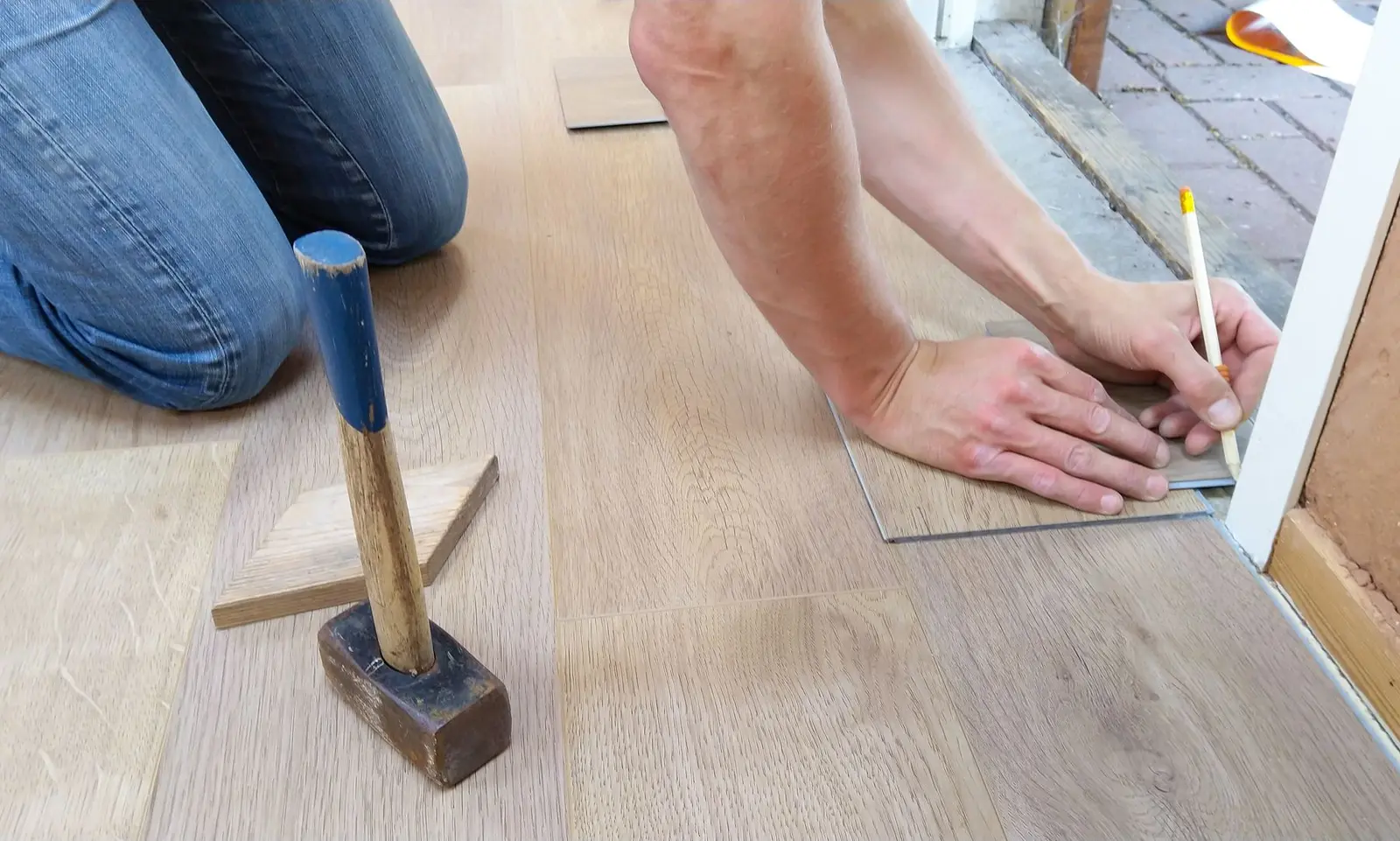 Handwerker zeichnet ein helles Laminatpaneel an einem Türrahmen passgenau an