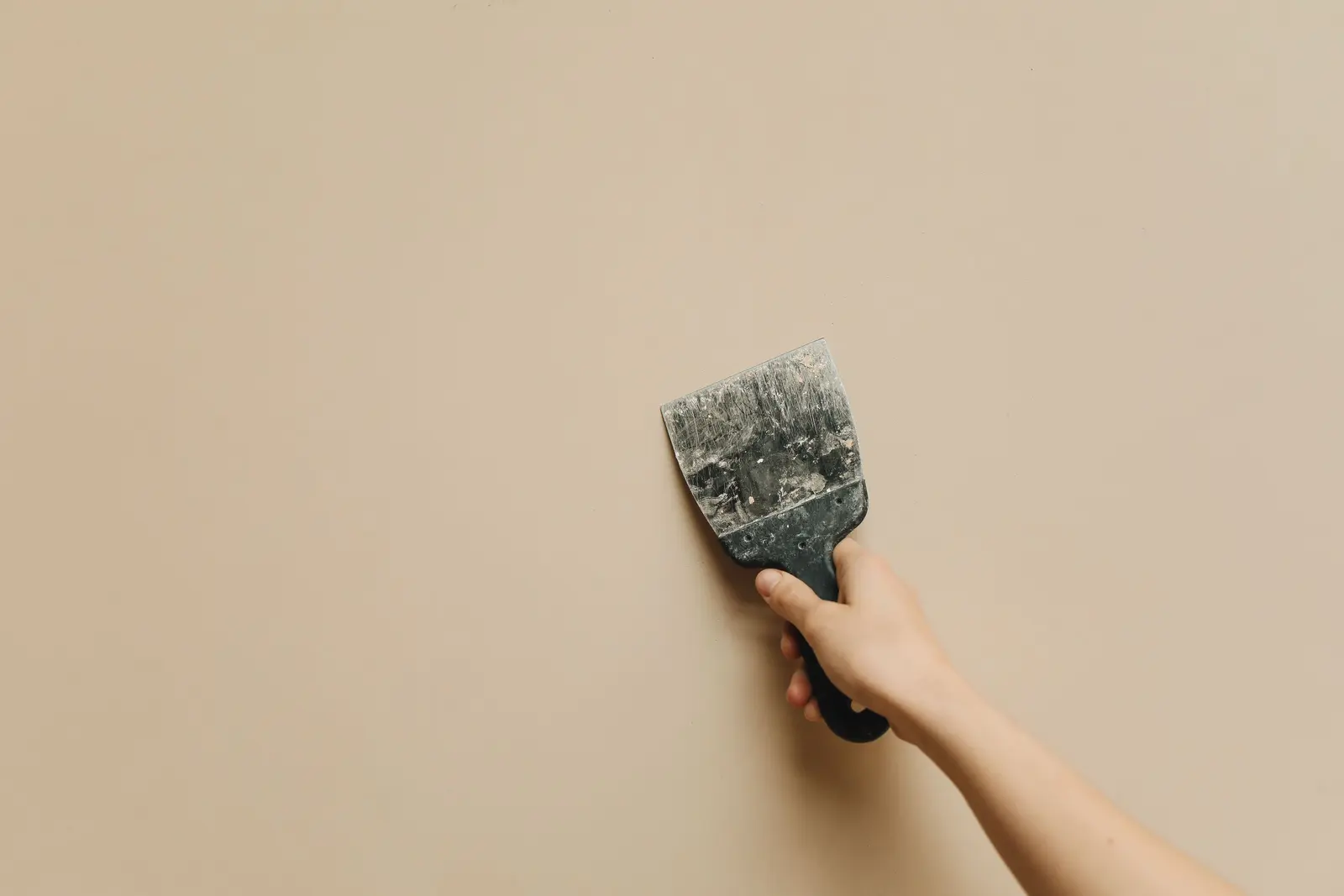 Hand mit breitem Tapetenschaber an einer Wand