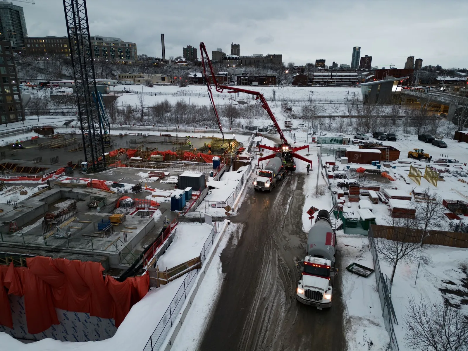 Verschneite Baustelle mit Baukran, Betonpumpe und geräumter Zufahrt