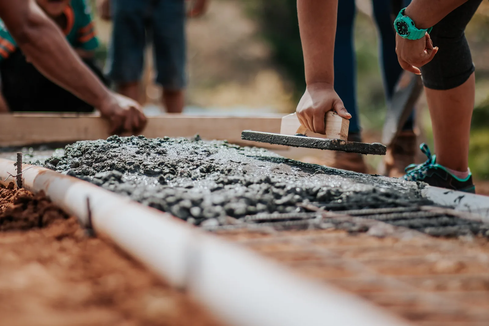 Bauarbeiter ziehen frisch eingebrachten Beton in einer Schalung mit Handwerkzeugen eben ab