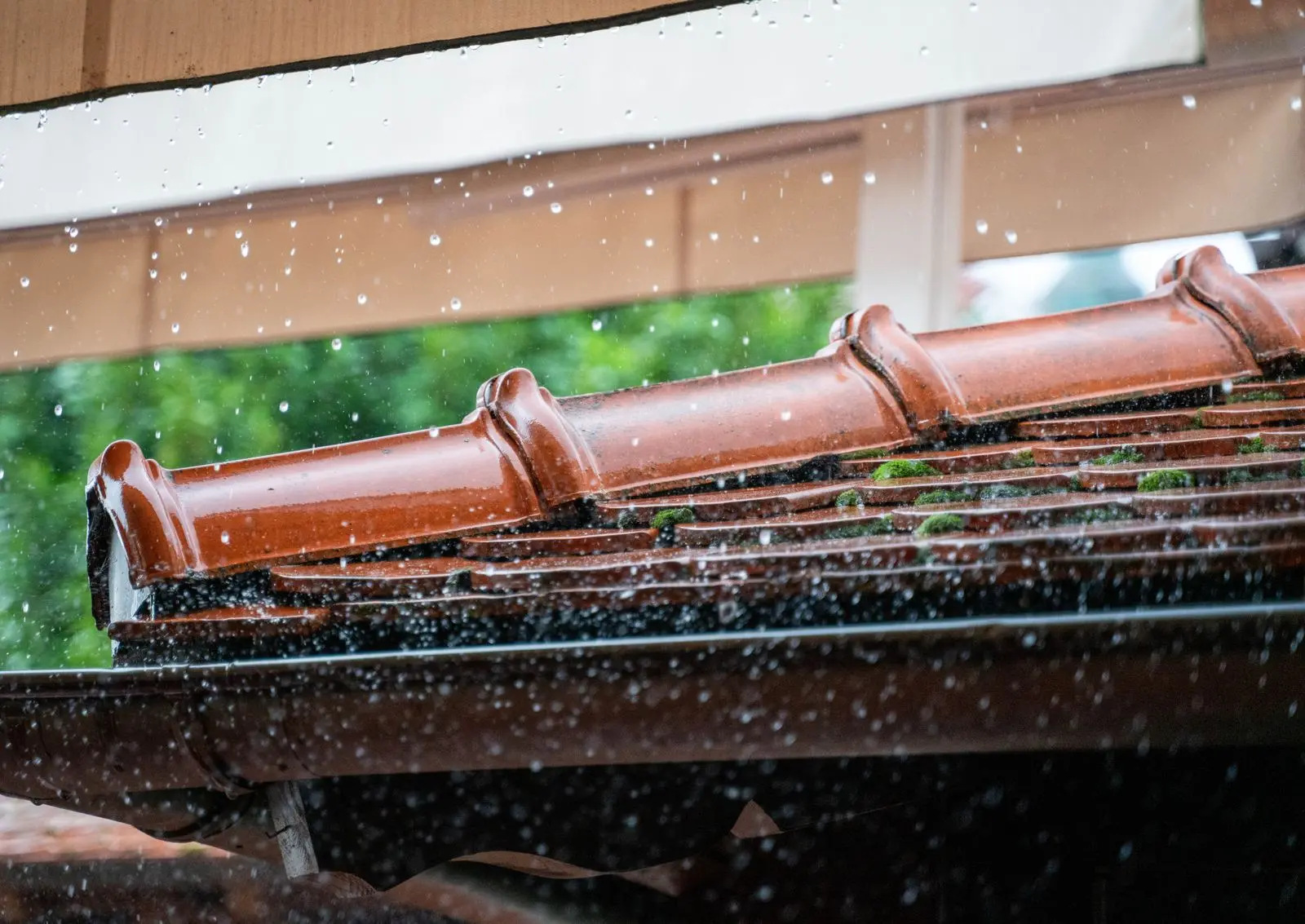 Regenwasser läuft von einem Ziegeldach in eine Dachrinne