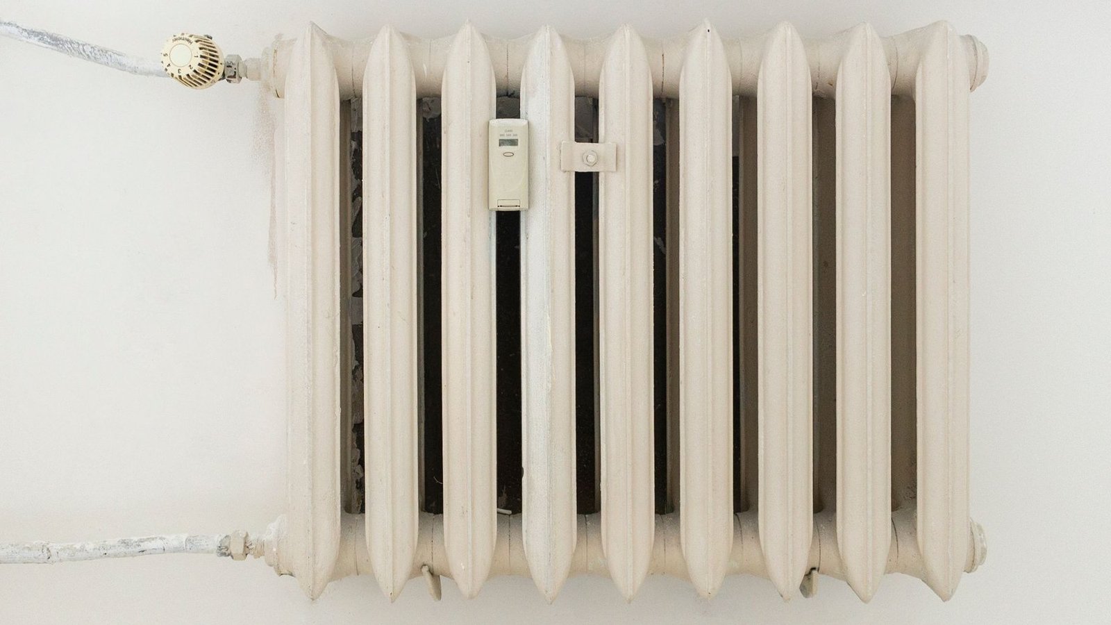 Cremefarbener Gussheizkörper mit Thermostatkopf an einer weißen Wand