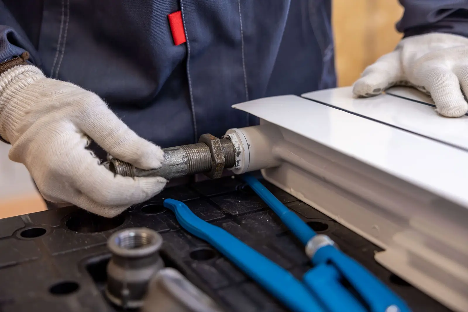 Behandschuhter Handwerker setzt eine Metallleitung an einem Heizkörper an
