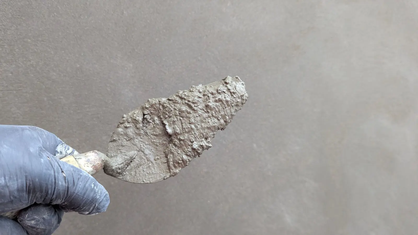 Behandschuhte Hand mit Kelle und frischer Spachtelmasse vor einer verputzten Wand