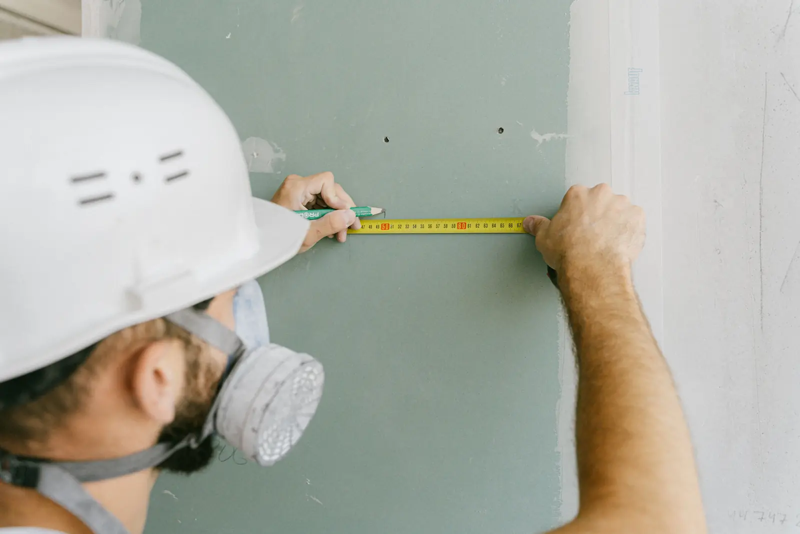 Handwerker vermisst mit Maßband und Bleistift eine grüne Gipskartonwand