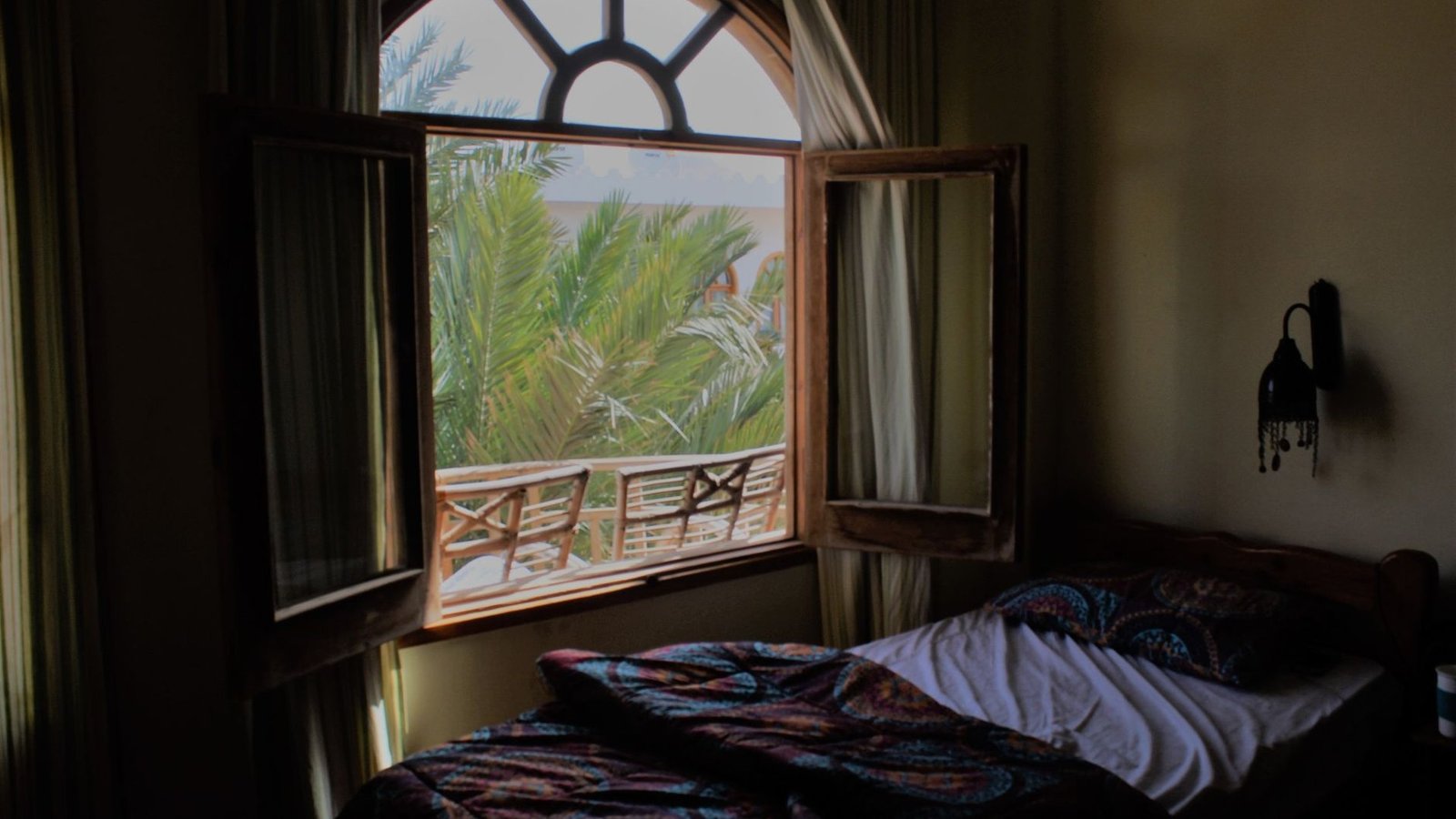 Weit geöffnetes Holzfenster in einem Schlafzimmer mit Blick auf Palmen und Balkon