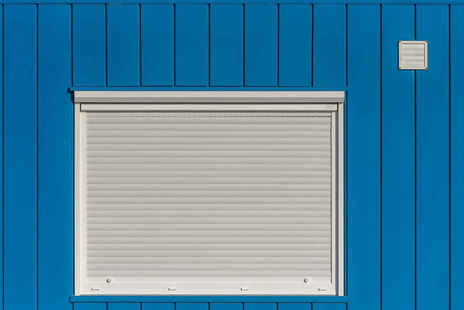 Geschlossener weißer Rollladen in einer blauen Außenwand