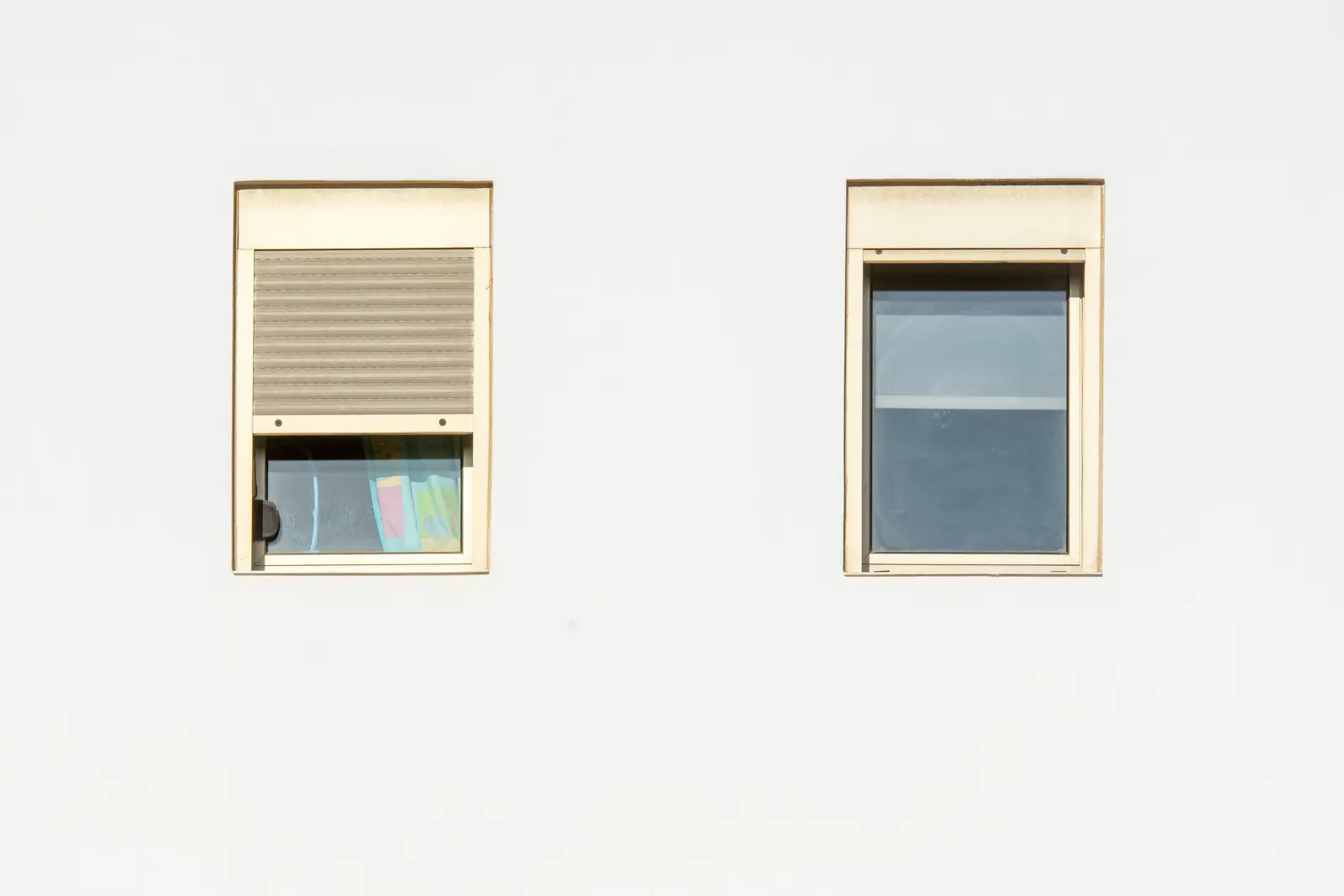 Zwei Fenster an einer hellen Fassade, eines mit teilweise geschlossenem Rollladen