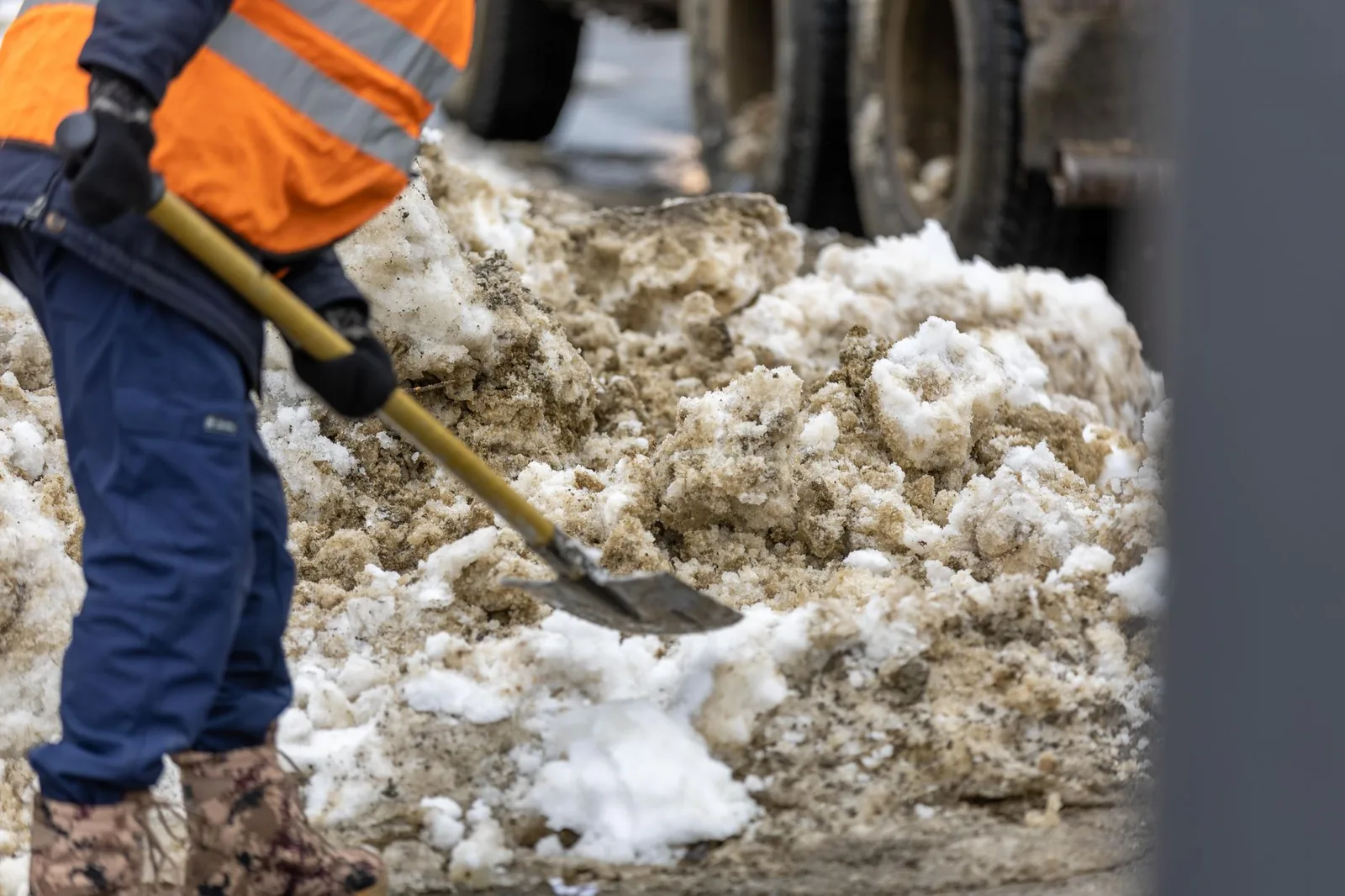 Arbeiter in Warnkleidung räumt Schnee von einem Baustellenweg