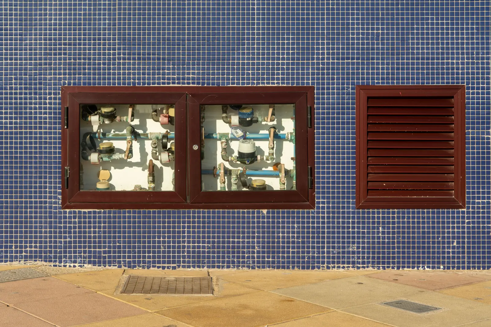 Wasserzähler und Leitungen hinter zwei geöffneten Klappen in einer gefliesten Wand