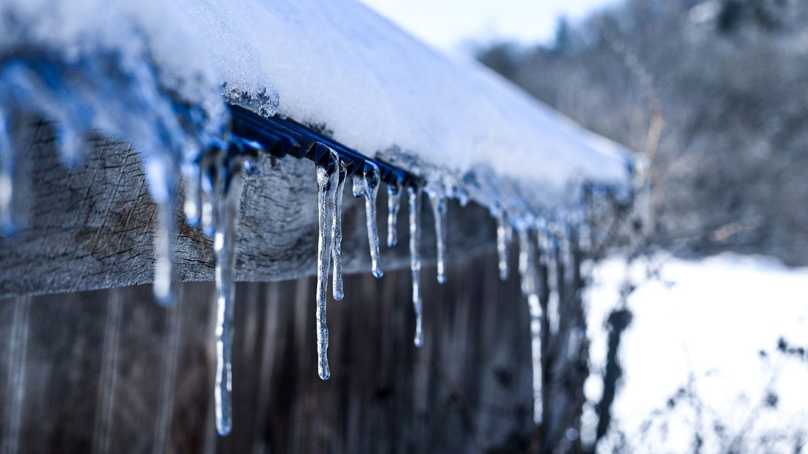 Eiszapfen hängen von einem schneebedeckten Dach über einer verwitterten Holzwand